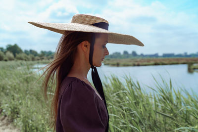 Rear view of woman wearing hat standing by lake
