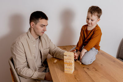 Father and son sitting together at home and playing with wooden blocks. jenga game.