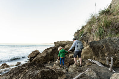 Father and son holding hands walking on rocks near ocean