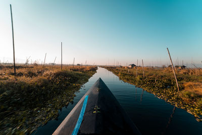 Road by canal against clear blue sky