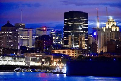 Illuminated buildings by river against sky at night