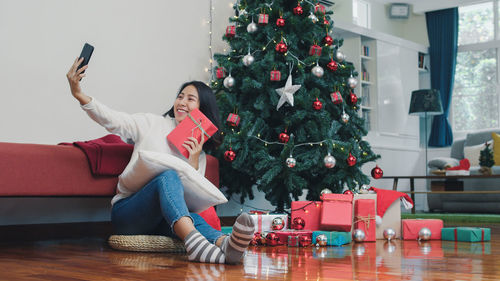 Full length of woman sitting on christmas tree at home