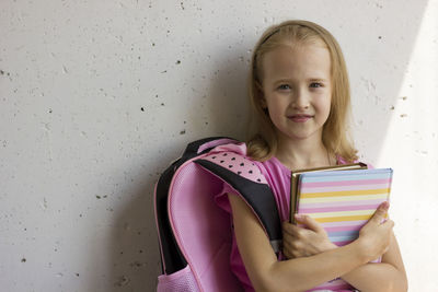 Back to school. blonde cute girl with a pink backpack and books stands against the background 