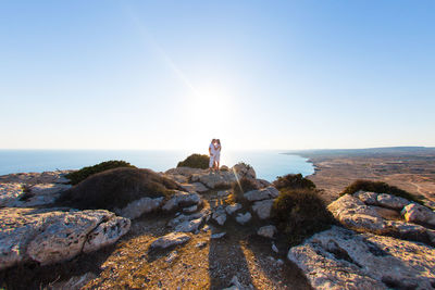 Rear view of woman standing on rock against sky