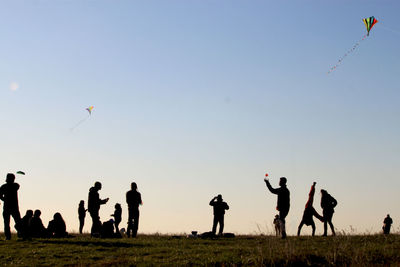 Silhouette people flying on field against clear sky