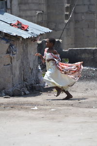 Side view of girl running on road against building during sunny day