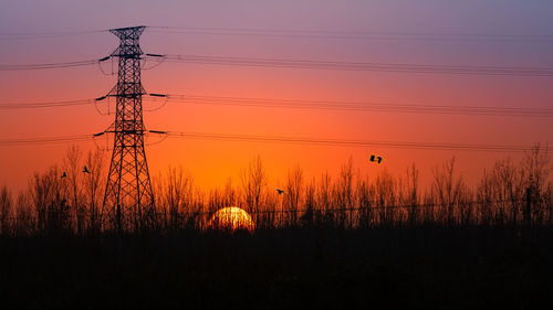 Silhouette electricity pylon on field against sky during sunset