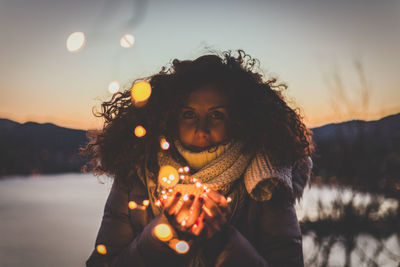 Portrait of woman holding illuminated lights against sky