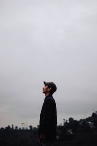 Side view of young man looking at camera against sky