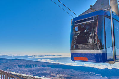 Overhead cable car on snowcapped mountains against blue sky