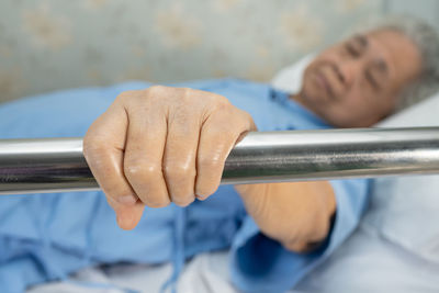 Senior woman lying down on bed while holding railing in hospital