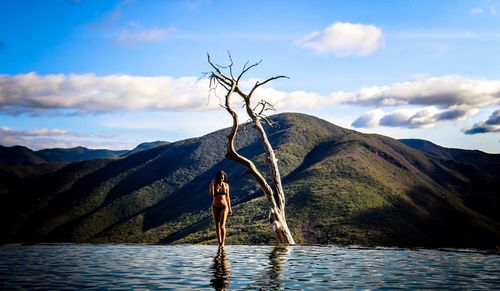 Full length of woman standing by infinity pool against sky