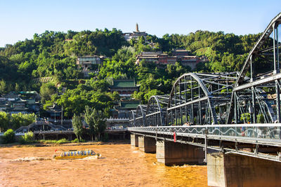 Bridge over river by buildings against sky