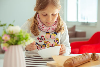 Girl having breakfast with bread while sitting on table