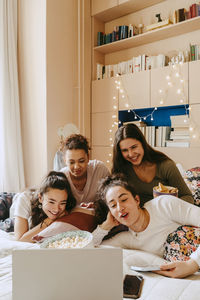 Happy multiracial female friends watching movie together on laptop at home