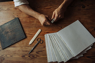 Hands, sheets of paper, wooden panel, scissors on wooden surface