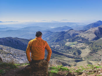 Rear view of man standing on mountain against sky