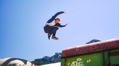 Low angle view of man jumping on train against clear blue sky