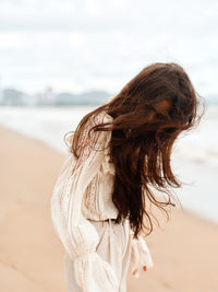Side view of young woman at beach against sky