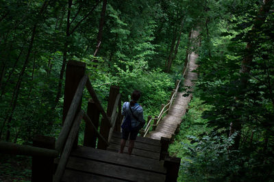 Rear view of woman walking on footbridge in forest