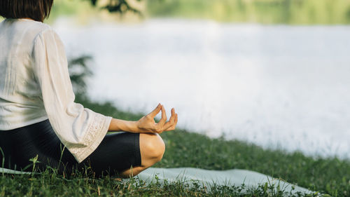 Young woman sitting in lotus position and practicing meditation near water in the nature