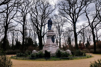 Statue by bare trees in park against sky