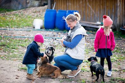 Happy family-mother with children hugging and feeds pets dogs, cats and goats in countryside farm