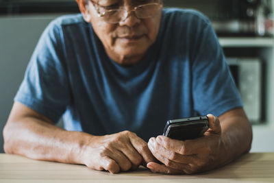 Midsection of man using mobile phone while sitting on table