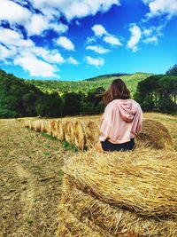 Rear view of woman sitting on hay bales at field