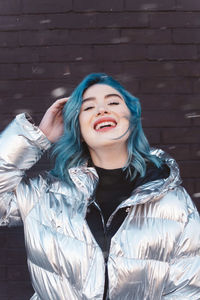 Laughing woman wearing coat against brick wall during winter