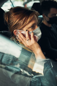 Woman talking on phone using smartphone sitting in a car wearing the face mask to avoid virus