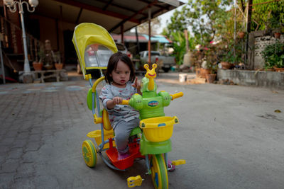 Portrait of cute girl riding tricycle on footpath