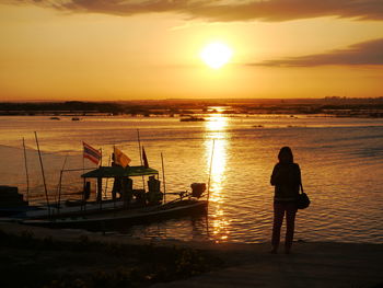 Full length rear view of woman at beach by moored boat against sky during sunset