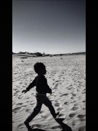 Rear view of boy on beach against clear sky