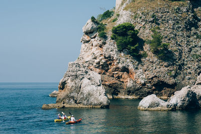 People on rock by sea against clear sky