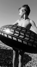 Boy in inflatable ring standing against clear sky