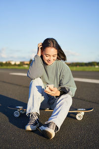 Young woman sitting on road against clear sky