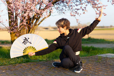 Young caucasian woman posing a wushu martial art posture in a sunny day, a pink tree in background