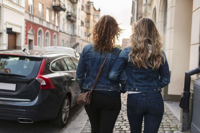 Rear view of mother and daughter walking at roadside in city