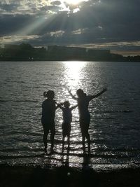 Silhouette people standing by sea against sky during sunset