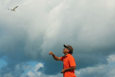 Low angle view of man looking at seagull flying at sky