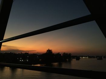 Silhouette city by river against sky during sunset