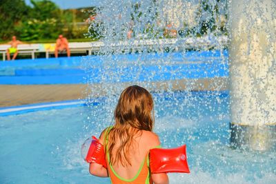 Happy little girl enjoying summer day in the swimming pool. girl going to a sprinkler in spray pool