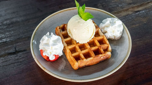 A image of a freshly prepared waffle accompanied by whipped cream and ice cream