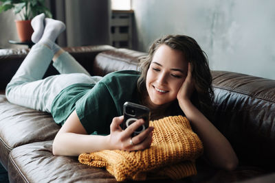 Young woman using phone while sitting on sofa at home