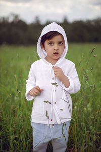 Boy child in a green field in summer in a white shirt with a hood made  linen in shorts and sandals