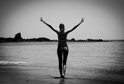 Woman with arms raised standing at sea shore against clear sky