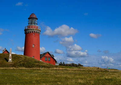 Lighthouse on field against cloudy sky