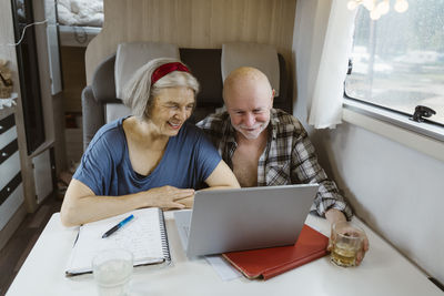 Happy senior couple sitting with laptop at table in camper van