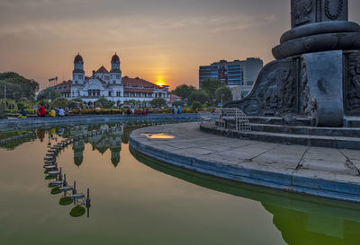 Reflection of building in lake against sky during sunset